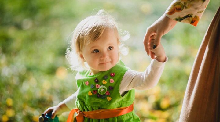 Girl In Green Dress With Love Heart Buttons Holding Mothers Hand And Toy In Other Hand