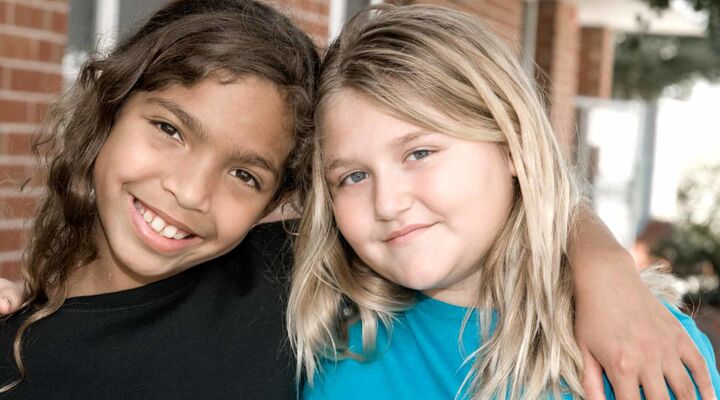 Aboriginal Girl Smiling With Arm Around Friend With Blonde Hair