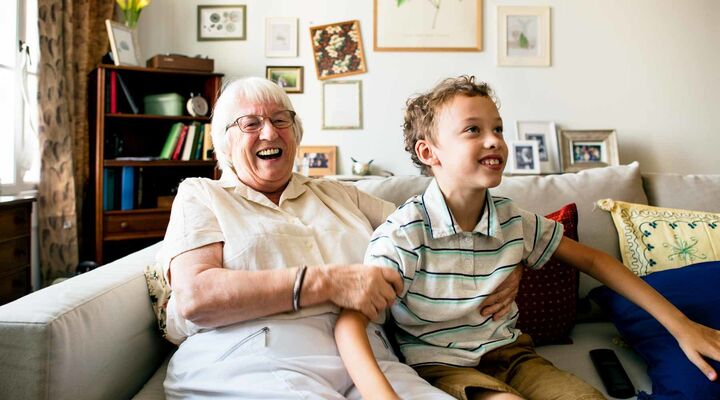 Grandmother On Light Grey Couch Holding Grandson In Arms Both Smiling